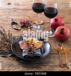 Tannenzapfen, gefallene Blätter und getrocknete Beeren Pflanze auf einer Serviette in einem Teller mit zwei Gläser Wein und Granatäpfel Stockfoto