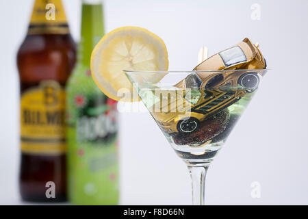 Miniatur-Autos und ein Autoschlüssel sinken nach unten in den Alkohol in ein Cocktailglas unscharf Stockfoto