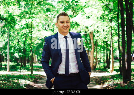 Wunderschöne stilvolle elegante glückliche Bräutigam im Licht auf einem Hintergrund von schönen sonnigen Bäumen in einem Wald stehen Stockfoto