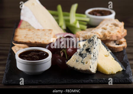 Eine Käseplatte auf Schiefer mit Chutney, Cheddar, Stilton Käse, Cracker, Brie, Trauben und Sellerie. Stockfoto