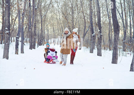 Glücklicher Mann Reiten Kinder auf Schlitten beim Aufenthalt in Winter park Stockfoto