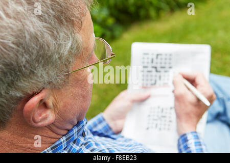 Ältere Mann tut Kreuzworträtsel im Garten Stockfoto