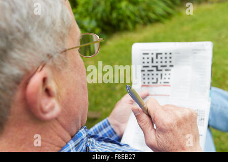 Ältere Mann tut Kreuzworträtsel im Garten Stockfoto