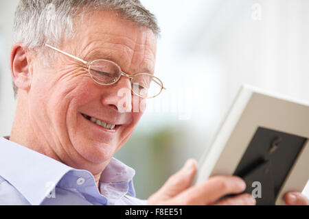 Lächelnde Senior Man Looking At Foto im Rahmen Stockfoto