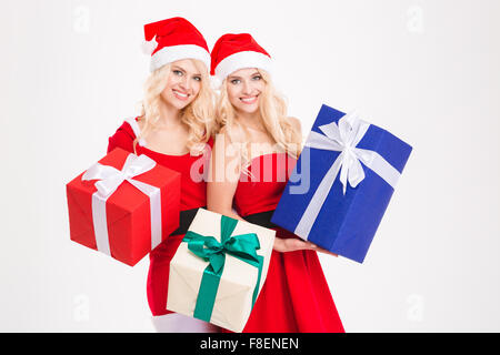 Zwei attraktive glücklich Schwestern Zwillinge im Weihnachtsmann-Kostüme und Hüte holding präsentiert auf weißem Hintergrund Stockfoto