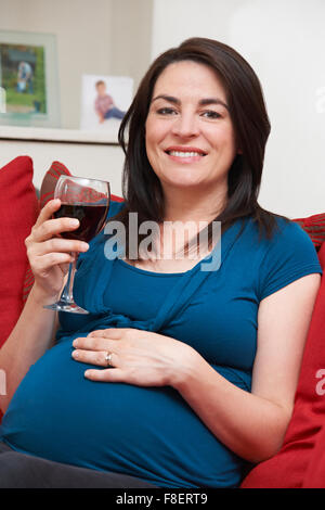 Lächelnde schwangere trinken Glas Wein zu Hause Stockfoto