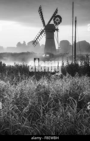 Atemberaubende Landschaft mit Windmühle und Fluss bei Sonnenaufgang am Sommermorgen in schwarz / weiß Stockfoto