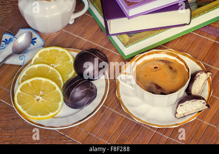Auf dem Tisch eine Tasse schwarzen Kaffee, Milch, Süßigkeiten, Zitrone. Die Aussicht von oben. Stockfoto