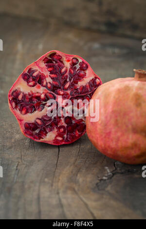 Ganze und einen halben Granatapfel auf einem rustikalen Holztisch Stockfoto