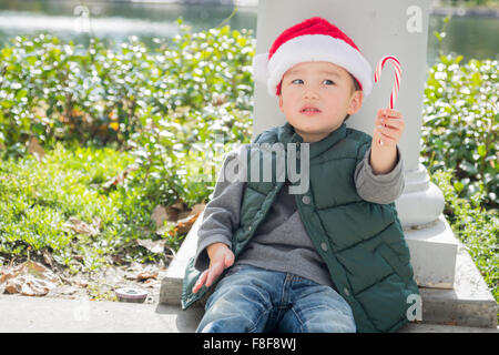 Süße Mischlinge Boy Sitting Weihnachten Santa Hut und genießen eine Zuckerstange. Stockfoto