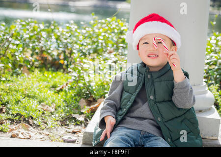 Süße Mischlinge Boy Sitting Weihnachten Santa Hut und genießen eine Zuckerstange. Stockfoto