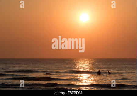 Sonnenuntergang über dem Meer in Perranporth, Cornwall England mit Surfer im Meer. Stockfoto