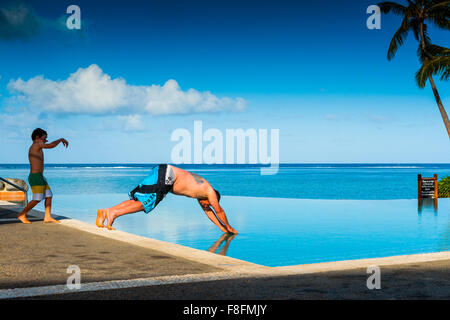 Ein Vater taucht in einem Infinity-pool, während sein Sohn Uhren auf der tropischen Insel der Fidschi-inseln im Südpazifik. Stockfoto
