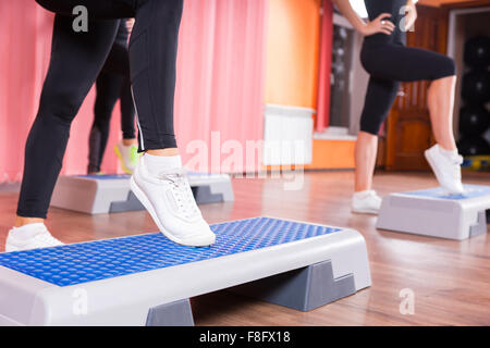 Nahaufnahme von Frau trägt weiße Turnschuhe tun Toe Tippen Sie auf Schritt-Plattform in Aerobic-Übungen Klasse mit Gruppe von Frauen im Hintergrund im Tanzstudio. Stockfoto