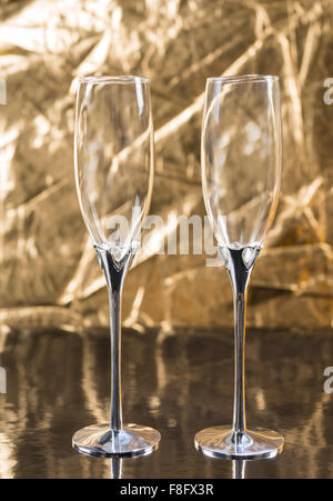 Zwei leere kristallklare stemmed Querflöte Gläser zum Trinken Champagner auf einer besonderen Veranstaltung oder Feier auf einer polierten goldenen Oberfläche angeordnet. Stockfoto