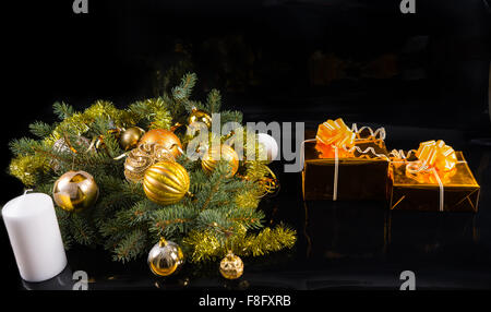 Festlichen Stillleben - paar Geschenke in Gold mit Bögen auf schwarzem Hintergrund mit weißen Kerze und immergrünen Zweigen geschmückt mit Christbaumkugeln und Gold Flitter Kranz mit textfreiraum gewickelt. Stockfoto