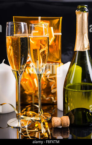 Nahaufnahme von entkorkt Flasche Champagner mit zwei gefüllten Gläsern in Still Life with Gold Weihnachtsgeschenke, weiße Kerzen und gewellten Band. Stockfoto