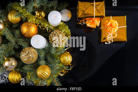 Unter dem Motto Weihnachten Goldgrund mit zwei dekorative Geschenke, Kerzen und eine Anordnung von Kugeln und Tannenzweigen, Draufsicht auf schwarz mit Exemplar. Stockfoto