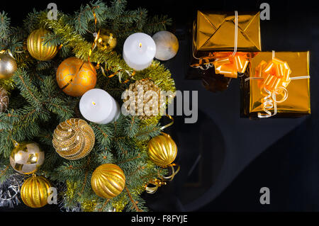 Gold unter dem Motto Weihnachten Stillleben mit Kugeln und Ornamente auf grünen Zweige umliegenden zwei brennende Kerzen und zwei Flöten romantische Champagner, Draufsicht auf schwarz. Stockfoto