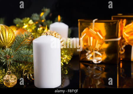 Weiße Weihnachten oder Advent Kerze mit einer Anordnung von Tannenzweigen und goldenen Verzierungen mit einem Luxus gold Geschenk neben über schwarz mit Exemplar. Stockfoto