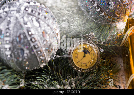 In der Nähe bis von altmodisch Taschenuhr hängen Schnee bedeckt Zweige immergrüner Baum mit funkelnden silberne Weihnachtskugeln geschmückt. Stockfoto