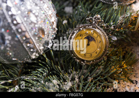 In der Nähe bis von altmodisch Taschenuhr hängen Schnee bedeckt Zweige immergrüner Baum mit funkelnden silberne Weihnachtskugeln geschmückt. Stockfoto