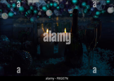 Licht von Flammen der brennenden Kerze Dochte schwach leuchtenden Flasche und Gläser Champagner in verschneiten Umgebung mit funkelnder Weihnachtsschmuck. Stockfoto