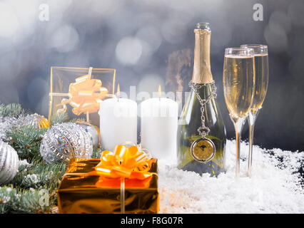 Festlichen Stillleben - Taschenuhr baumelte Flasche Champagner neben zwei gefüllte Gläser auf Schnee bedeckte Oberfläche mit Geschenken, Kerzen und Weihnachten Dekorationen in diffusem Stillleben. Stockfoto