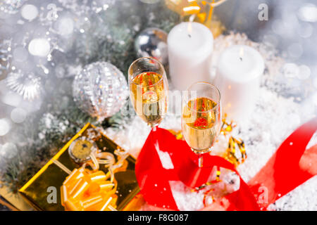 High Angle festlichen Stillleben - paar gefüllten Sektgläsern auf Schnee bedeckt Oberfläche mit brennenden Kerzen, Gold Geschenke und glitzerndem Weihnachtsschmuck. Stockfoto