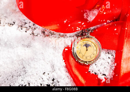 High Angle View of alte altmodische antike Taschenuhr ruht auf festliche rote Schleife und Schnee bedeckt Oberfläche mit textfreiraum - Geschenk und Time-Konzept-Image. Stockfoto