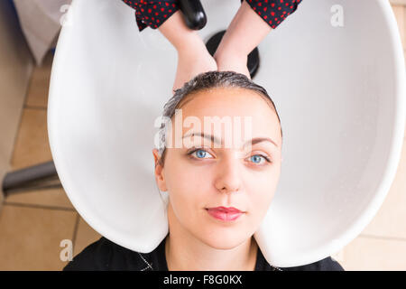 High Angle nahe Ansicht von junge Brünette Frau ohne Haare gewaschen von Stylistin im Waschbecken im Salon Spa zufrieden in die Kamera schauen. Stockfoto