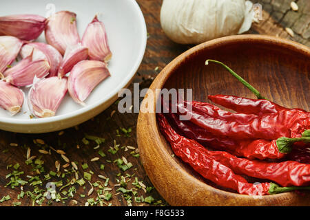 Getrocknete Chili in Holzschale umgeben von Knoblauch und Paprika auf alten Holztisch Stockfoto