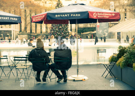 Paar sitzt am Bryant Park Citi Teich in New York City mit Weihnachtsbaum im Hintergrund während der Ferien Stockfoto