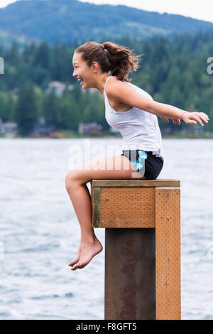 Gemischte Rassen Mädchen sitzen auf hölzernen Sockel am See Stockfoto