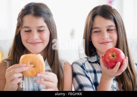 Kaukasische Zwillingsschwestern, die gesunde und ungesunde Snacks zu essen Stockfoto