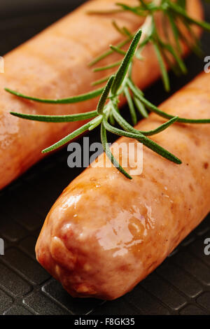 Rohwurst in Pfanne auf Holztisch umgeben von Zutaten Stockfoto