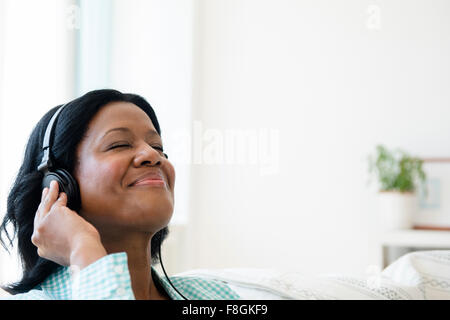 Schwarze Frau hören Kopfhörer auf sofa Stockfoto