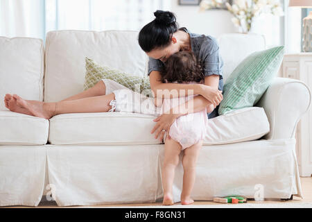 Mutter umarmt Baby-Tochter auf sofa Stockfoto