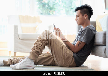 Asiatischer Mann mit Handy im Wohnzimmer