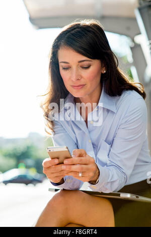 Kaukasische Geschäftsfrau mit Handy an Bushaltestelle Stockfoto