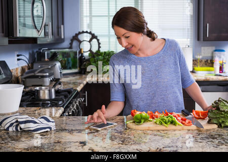 Gemischte Rassen Frau Lesung Rezept auf Handy in Küche Stockfoto