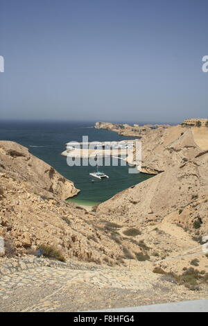 Berge mit Blick auf das Meer und ein Katamaran im Wasser der Küste von Muscat, Oman Stockfoto