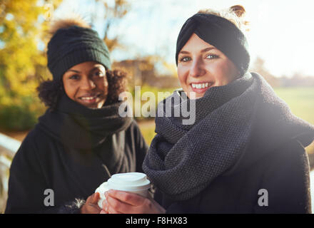 Zwei Freundinnen Blick in die Kamera und lächelnd halten Kaffee zu gehen Stockfoto