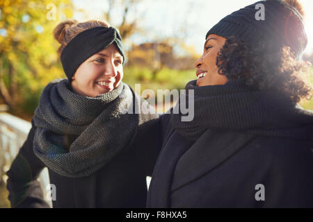Zwei Freundinnen sahen einander und lächelnd, während Sie im herbstlichen Park stehen Stockfoto