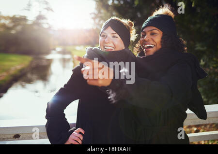 Zwei Freundinnen lachend an etwas beim Stehen in der Park gegen des Flusses. Stockfoto