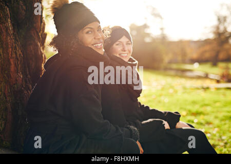 Zwei junge Frauen sitzen im herbstlichen Park und lächelt in die Kamera. Sonnig Stockfoto