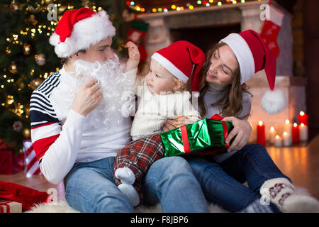Überrascht Kind schaut Papa weared Weihnachtsmann mit falschen Bart gegenübersitzt Weihnachtsbaum Stockfoto