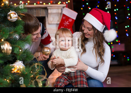 Glückliche Familie mit Kind dekorieren Weihnachtsbaum vor dem Kamin im Wohnzimmer Stockfoto