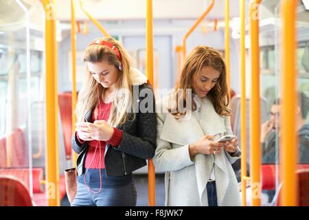 Zwei junge Frauen auf Zug, Rücken an Rücken mit smartphones Stockfoto
