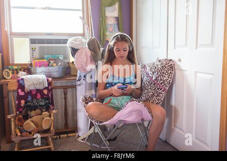 Teenager mit Smartphone auf Sessel im Schlafzimmer Stockfoto